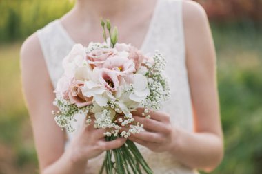 yeşil bir bahçede duran ve bir düğün buket çiçek ve yeşillik tutan bir elbise içinde gelin. Düğün gününde onunla renkli buket tutan kadın eller