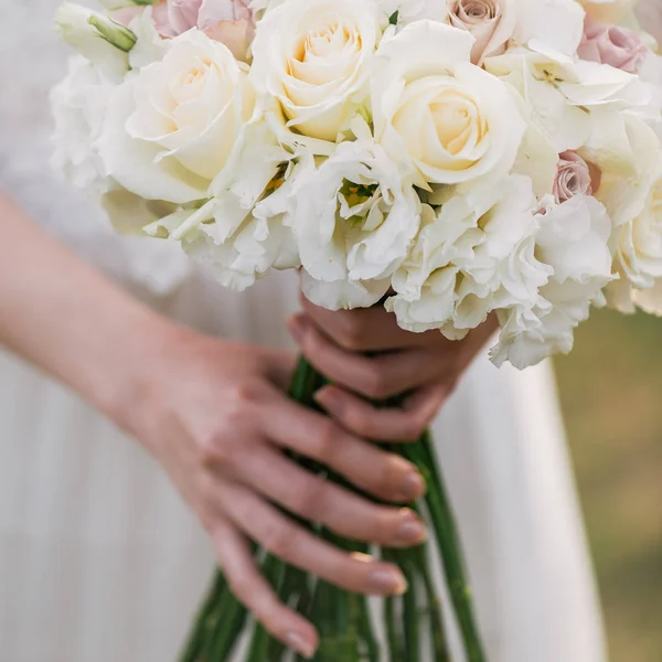Bruden i en klänning står i en grönskande trädgård och hålla ett bröllop bukett av blommor och grönska. Kvinna med färgglad bukett med henne händer på bröllopsdagen — Stockfoto
