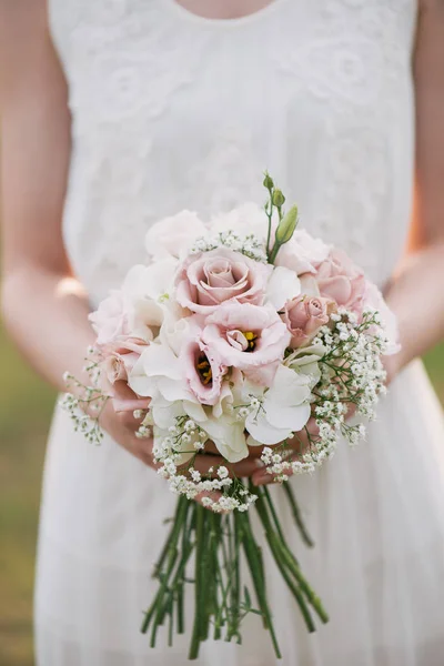緑の庭に立って、花と緑のウェディング ブーケ ドレスの花嫁。結婚式の日に彼女とカラフルな花束を持った女性の手します。 — ストック写真