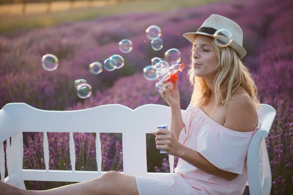 Красивая женщина, пускающая мыльные пузыри на открытом воздухе, милая молодая женщина, развлекающаяся на лавандовом поле — стоковое фото