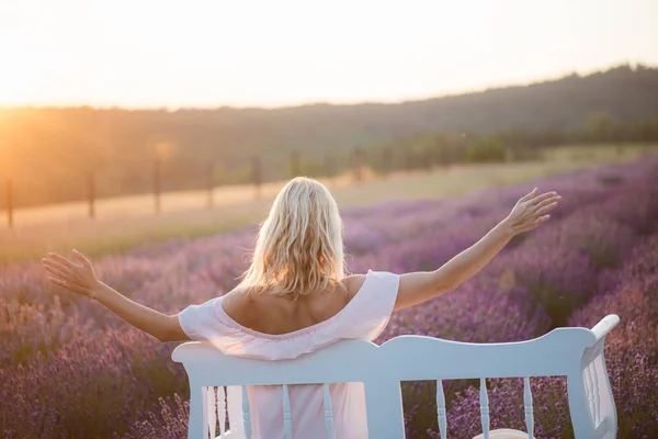 Achteraanzicht van jonge vrouw geniet van het leven op het bankje. Frisse lucht bij zonsondergang. — Stockfoto
