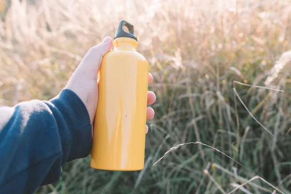 Botella amarilla en mano. Concepto de viaje. Mano sosteniendo frasco amarillo al aire libre . —  Fotos de Stock