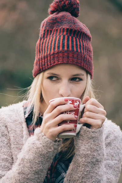 Woman drinking hot drink. Girl with red nails holding a hot cup of coffee or tea outdoors.