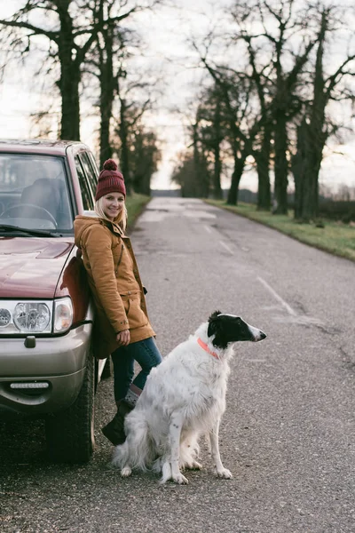 Travel with dog. Woman traveling with her dog. Standing by off road vehicle on the road.