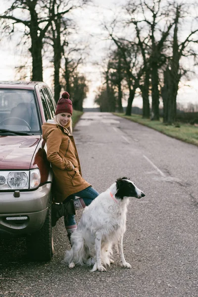 Travel with dog. Woman traveling with her dog. Standing by off road vehicle on the road.