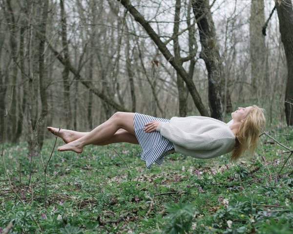 Красивая девушка висит над землей наслаждаясь в левитации в лесу
. 