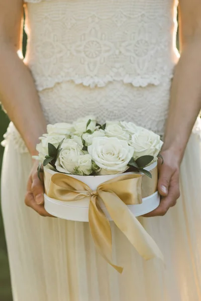 Rose box. Beautiful roses in white gift box with golden bow. Bride holding flower decoration on wedding day.