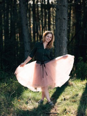 Beyaz etekli genç bir kadın gün batımında yeşil orman manzarasında dans ediyor..