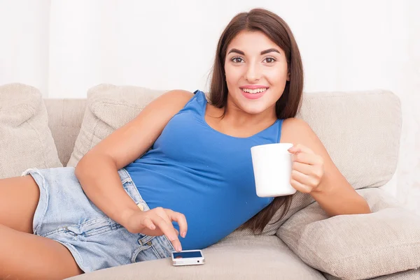 Kanepede oturan ve kahve içme genç esmer kadın — Stok fotoğraf