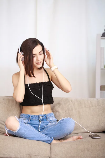 Frau hört Musik über Kopfhörer auf Sofa im Zimmer — Stockfoto