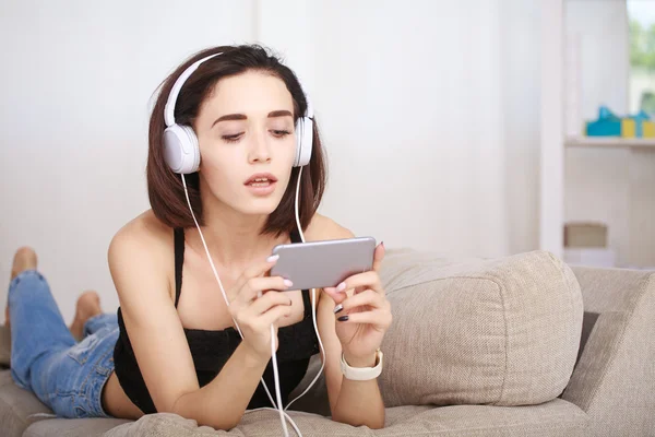 Woman listening music in headphones sitting on sofa in room — Stock Photo, Image