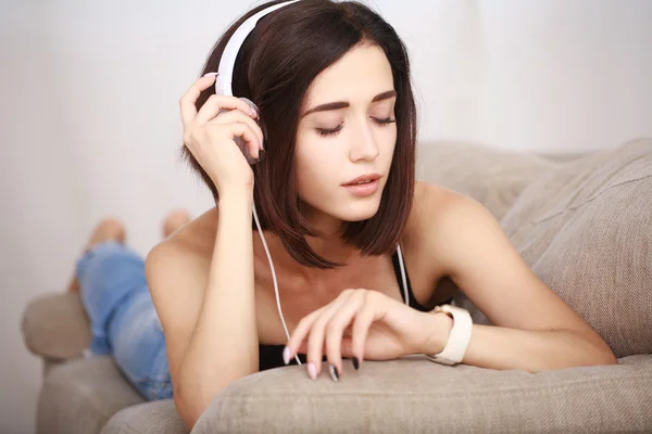 Nő zenehallgatás fejhallgató szobában a kanapén ül — Stock Fotó