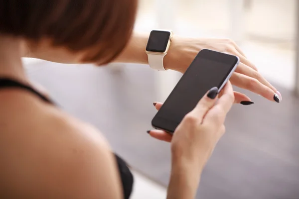 Nutzung ihrer Smartwatch und ihres Handys zu Hause im Wohnzimmer Stockbild