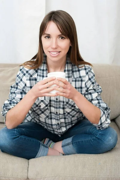 Woman sitting on couch in her living room and drinking coffee — Stock Photo, Image
