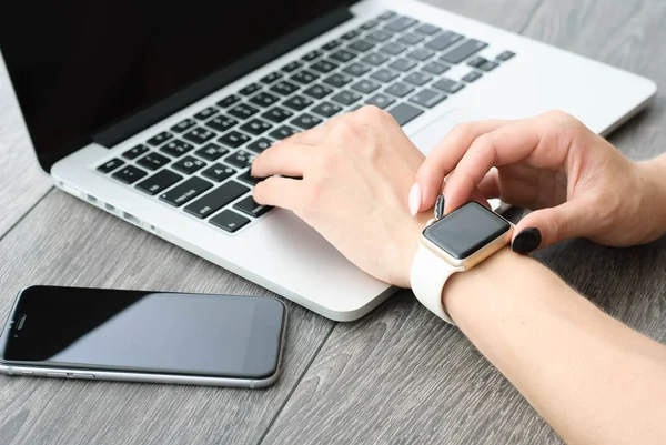 Main féminine avec smartwatch avec téléphone portable sur ordinateur portable — Photo