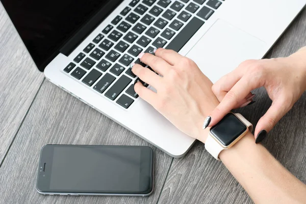 Main féminine avec smartwatch avec téléphone portable sur ordinateur portable — Photo