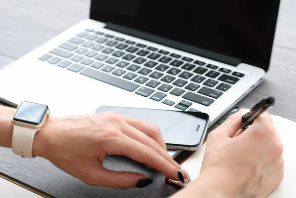 Main féminine avec smartwatch avec téléphone portable sur ordinateur portable — Photo