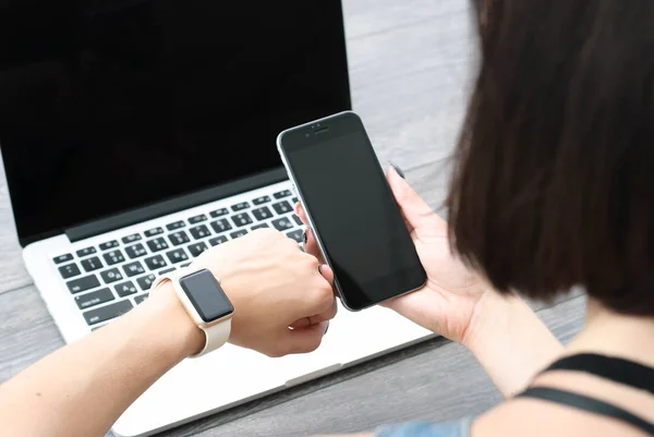 Mano femenina con smartwatch con teléfono móvil en el ordenador portátil — Foto de Stock