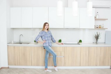 Genç güzel kız mavi kareli gömlek ve mavi jeans mutfakta duruyor. Ev iç