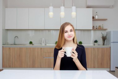 Kahve fincanı ile mutfakta oturmuş gülümseyen kadın. Uzun saçlı güzel kız.