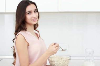 Sağlıklı kahvaltı. Genç güzel neşeli kadın tezgah üzerinde oturan ve gülümseyen bir kase mısır gevreği koyarak.