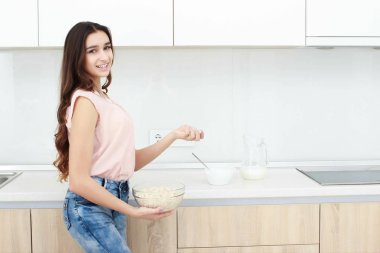 Sağlıklı kahvaltı. Genç güzel neşeli kadın tezgah üzerinde oturan ve gülümseyen bir kase mısır gevreği koyarak.