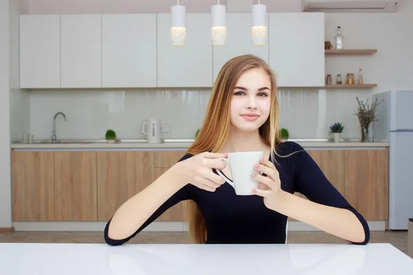 여자 커피 컵과 부엌에 앉아 웃 고입니다. 긴 머리를 가진 아름 다운 소녀. — 스톡 사진