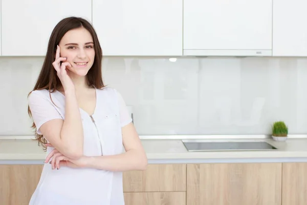 Brünette hausfrau in weiß in der küche sprechen auf dem handy — Stockfoto