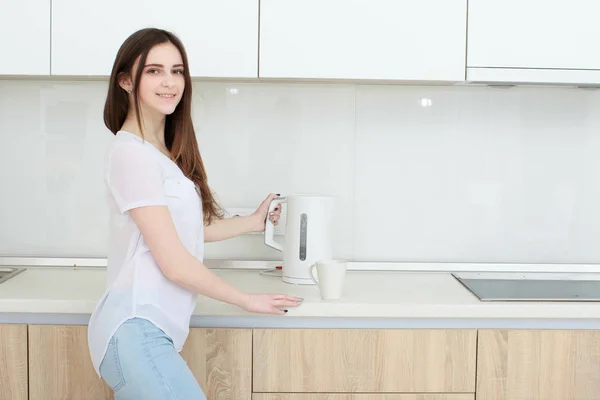 Menina bonita derrama água da chaleira na cozinha — Fotografia de Stock