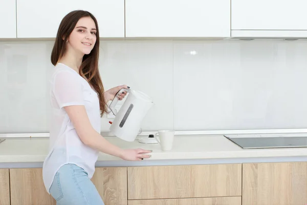 Menina bonita derrama água da chaleira na cozinha — Fotografia de Stock