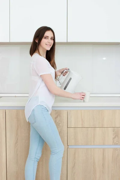 Красивая девушка наливает воду из чайника на кухне — стоковое фото