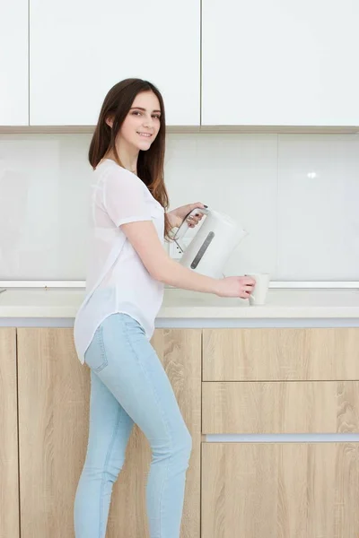 Menina bonita derrama água da chaleira na cozinha — Fotografia de Stock