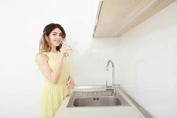 Mulher bonita segura um copo com água na cozinha — Fotografia de Stock
