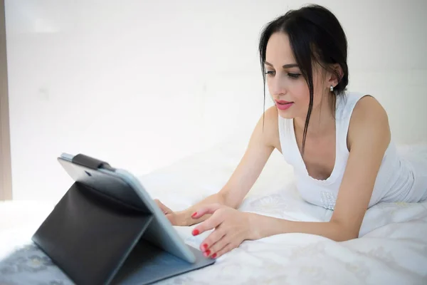Une femme se couche sur son lit à l'aide de sa tablette — Photo
