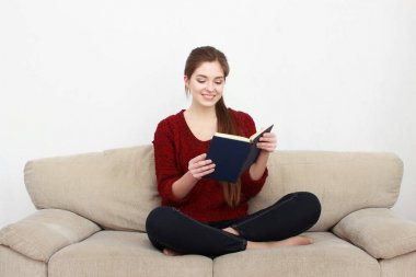 Kanepede kitap okuyan genç bir kadın.