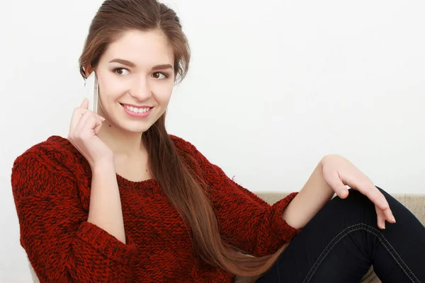 Giovane bella ragazza dai capelli rossi allegro in una giacca di jeans blu seduto sul divano a casa e parlando su un telefono cellulare . — Foto Stock