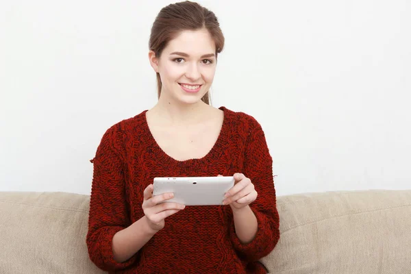 Belle fille utilise une tablette numérique et souriant tout en étant assis sur le canapé à la maison — Photo