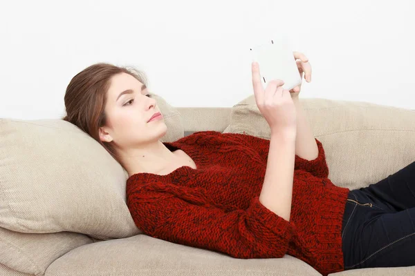 年轻美丽的开朗红头发的女孩穿着蓝色牛仔裤夹克坐在家里的沙发上，谈一部手机. — 图库照片