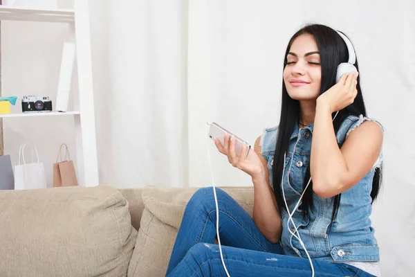 Una ragazza rilassata che riposa e ascolta musica con le cuffie sedute sul divano — Foto Stock