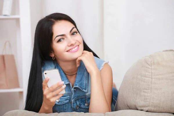 Jeune femme positive couchée sur le canapé et utilise un téléphone portable — Photo