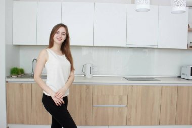 Genç ve güzel kadın mutfakta ayakta ve gülümseyen bir beyaz T shirt