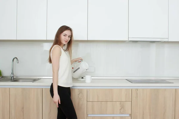 Hübsches Mädchen gießt Wasser aus dem Wasserkocher in der Küche — Stockfoto