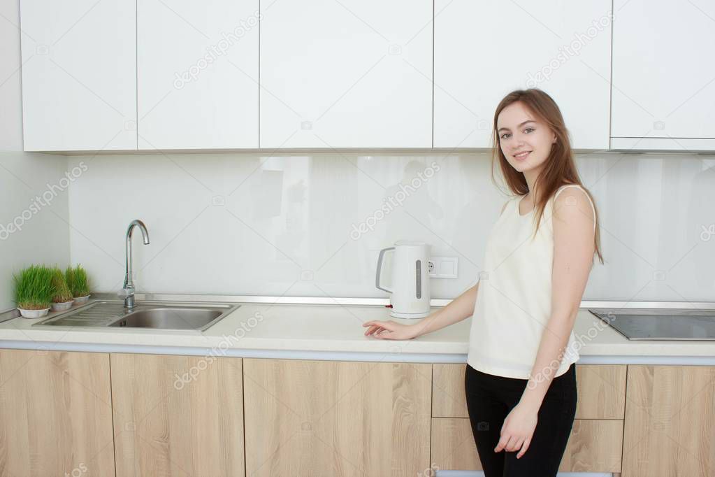 Pretty young woman In a white T shirt standing in kitchen and smiling