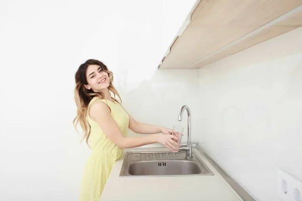 Mulher derramando vidro de água da torneira na cozinha — Fotografia de Stock