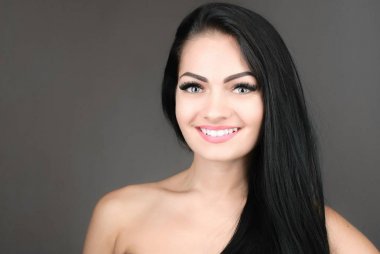 uzun kahverengi saçları gri arka plan üzerinde poz olan genç ve güzel bir kadın