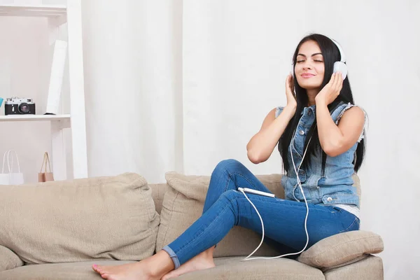 Una ragazza rilassata che riposa e ascolta musica con le cuffie sedute sul divano — Foto Stock