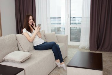 Evdeki koltukta oturmuş akıllı bir telefonla mesaj okuyan mutlu bir kız..