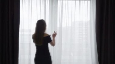 kadın örtüsünü açmak perde ve pencereden dışarı bakıyor