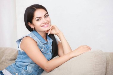 Rahat rahat esmer mavi hırka ve mavi kot pantolon kanepeye oturur