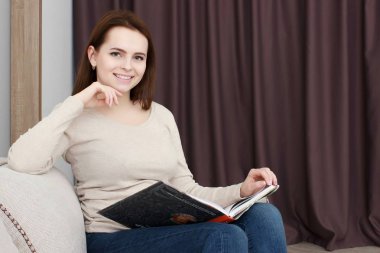 Güzel gülümseyen genç kadın kanepe üzerinde rahatlatıcı bir kitap zevk